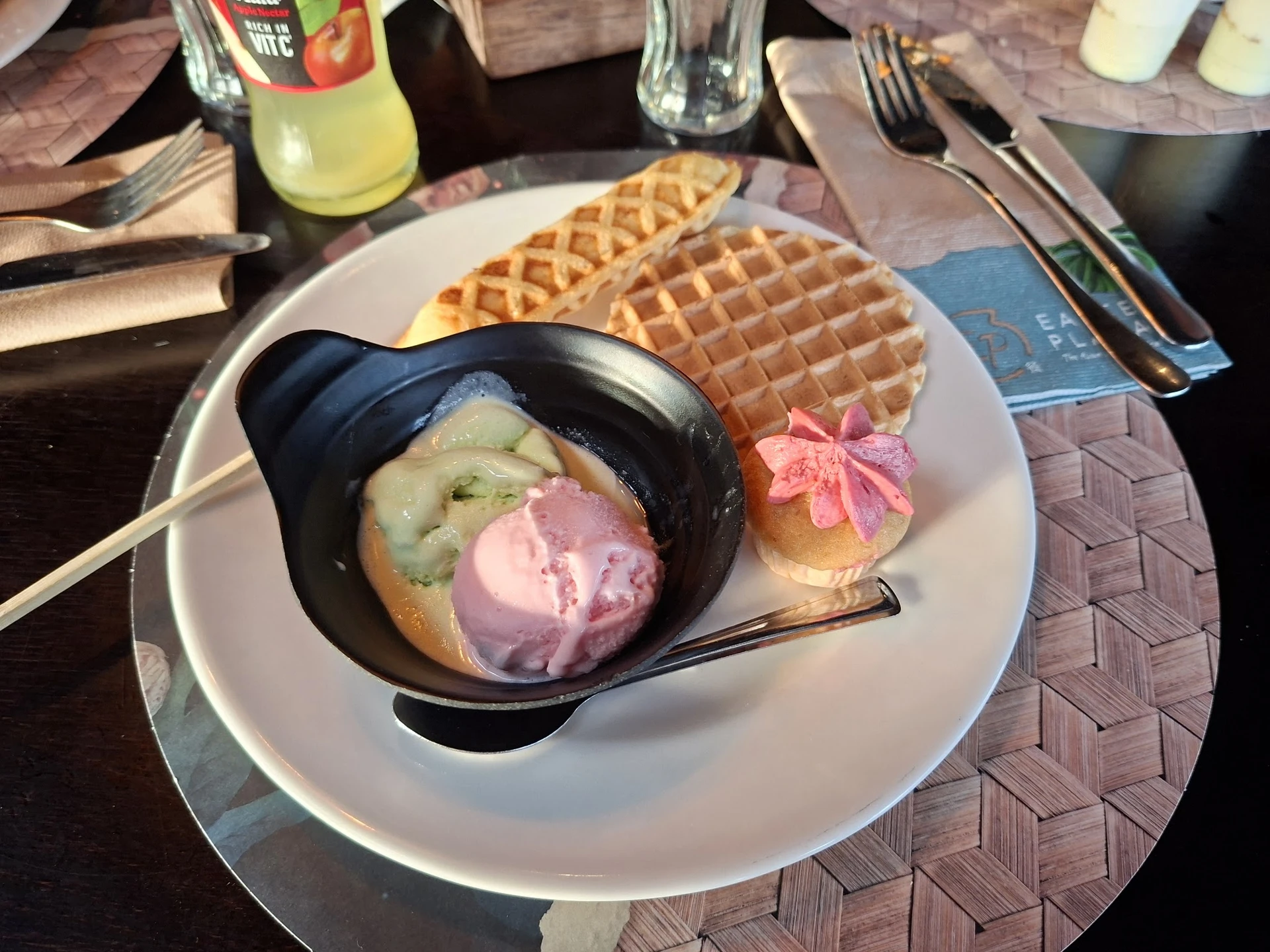 Bord met wafels en roze roomijs in zwarte kom, met drank op tafel