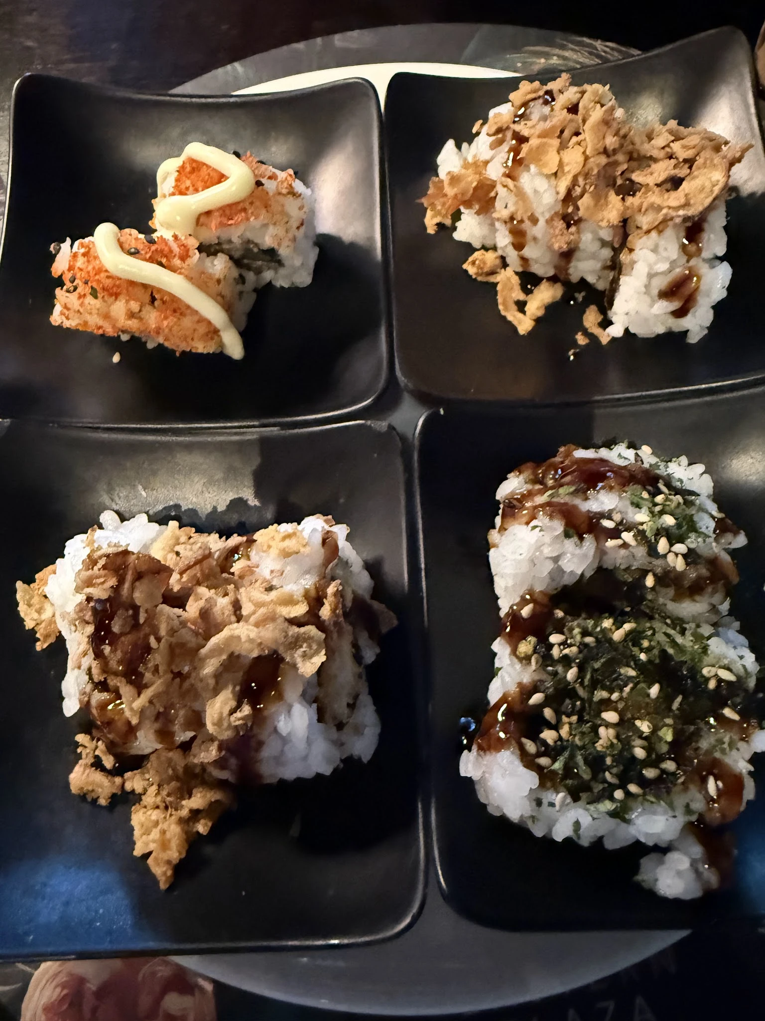 Vier sushi-rollen op zwarte borden, afgewerkt met saus en toppings