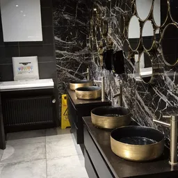 Vier decoratieve schalen met zwarte en gouden afwerking op zwarte plank tegen marmeren wand
