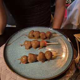 Drie spiesjes met bruine ballen en rode accenten op een grijsblauwe bord, serveergereed