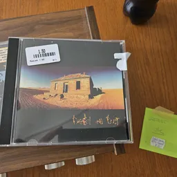 CD met desert-landschap op hoes en gouden schrift, op houten tafel naast prijsstickers