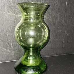 Groene glazen vaas met bulbeuze vorm tegen grijze achtergrond