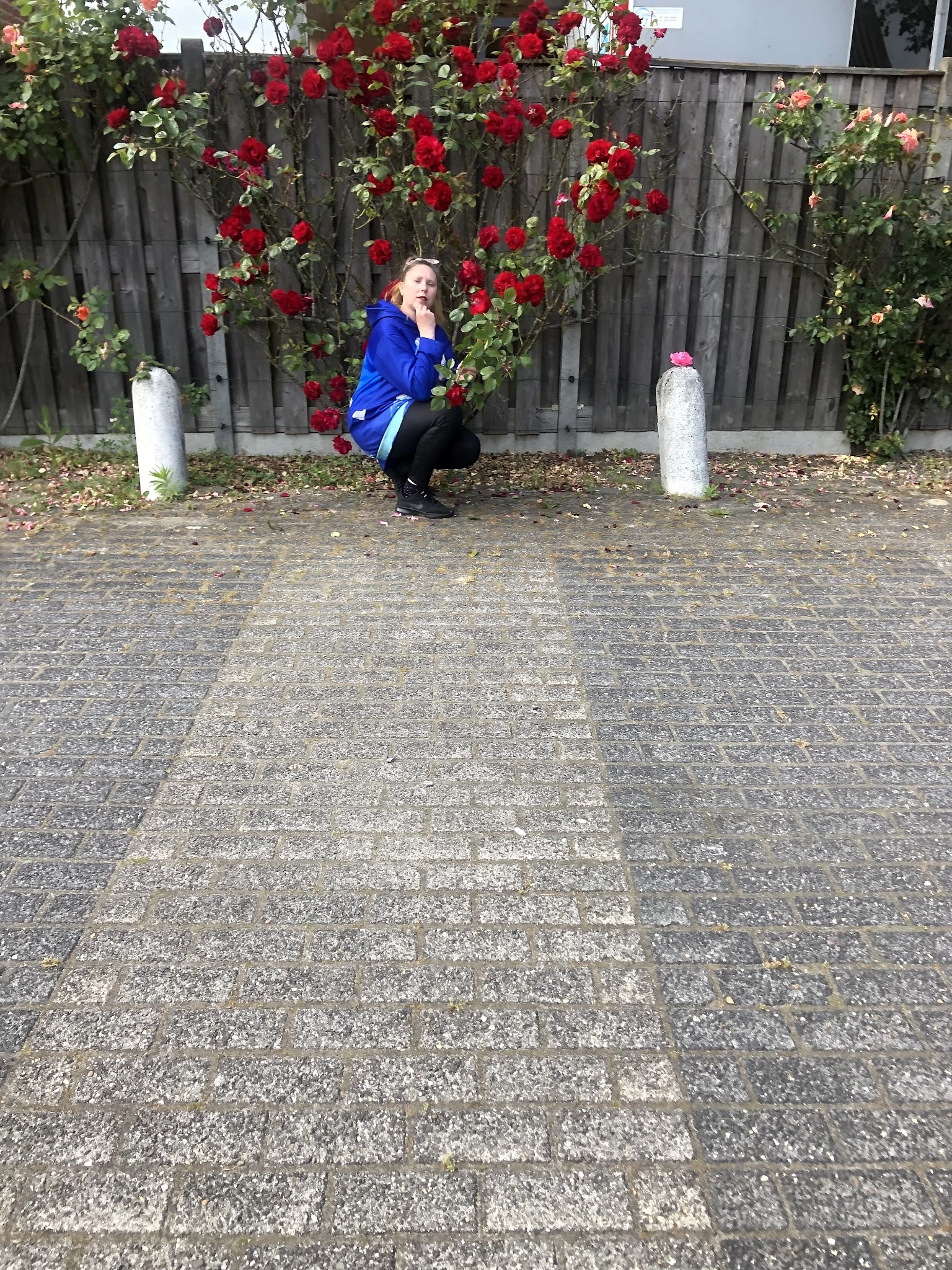 Voorkant van kringloopwinkel met bloemen in bakken, persoon in blauwe jas hurkt neer op tegels