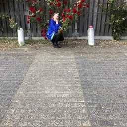 Voorkant van kringloopwinkel met bloemen in bakken, persoon in blauwe jas hurkt neer op tegels