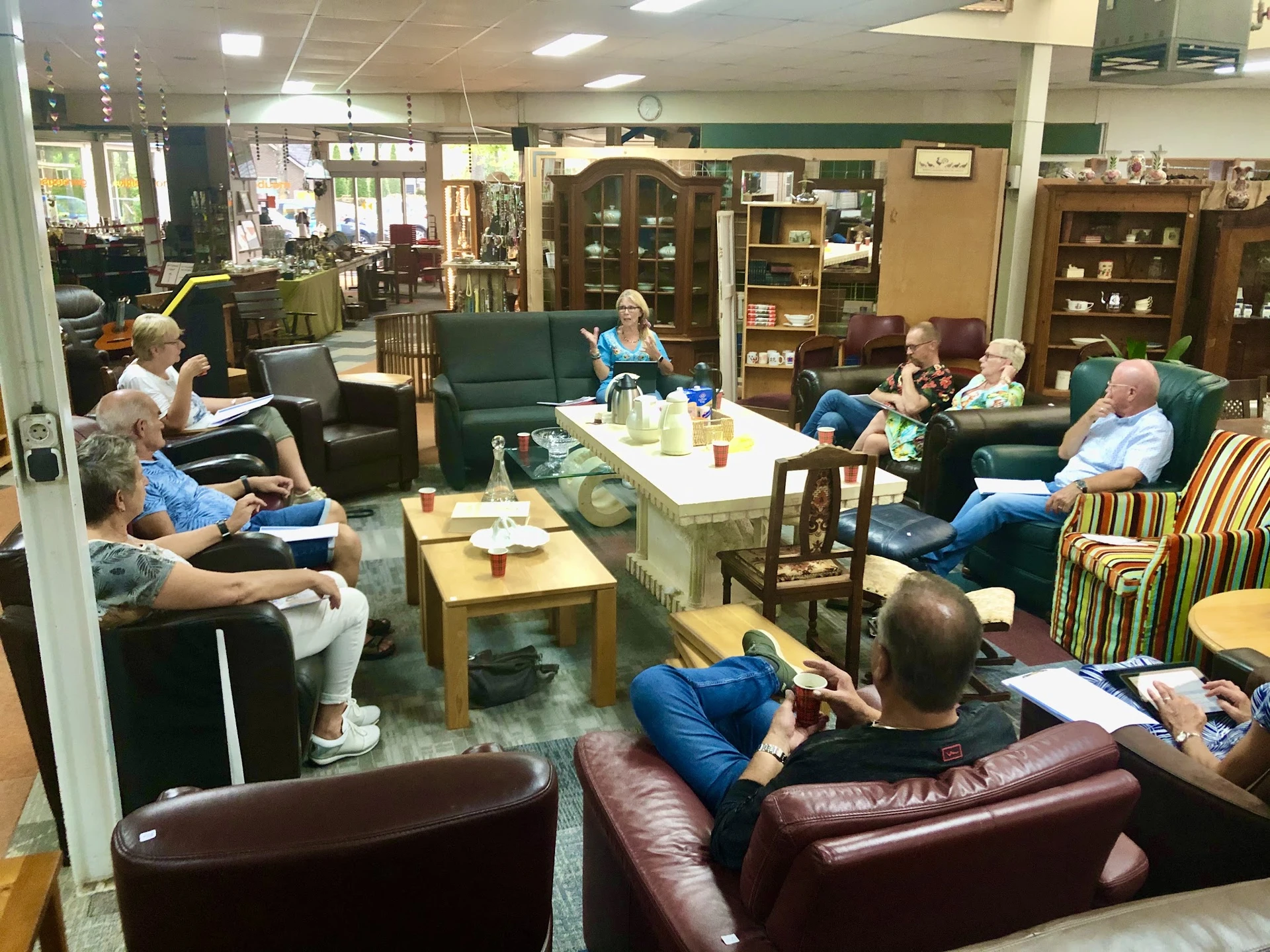 Groep bezoekers zit op verschillende stoelen en banken in een gezellige zithoek met tafels, drinken en hapjes
