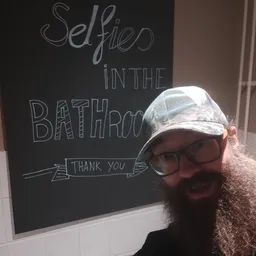 Man met baard, bril en pet poseren voor een schoolbord met handgeschreven tekst