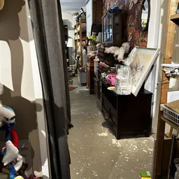 Smalle winkelgang met stellingen, kleding en spullen aan beide zijden, zonnicht door raam