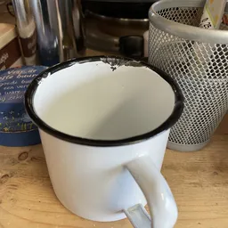 Witte emaille mok met zwarte rand, gedeeltelijk gevuld met vloeistof