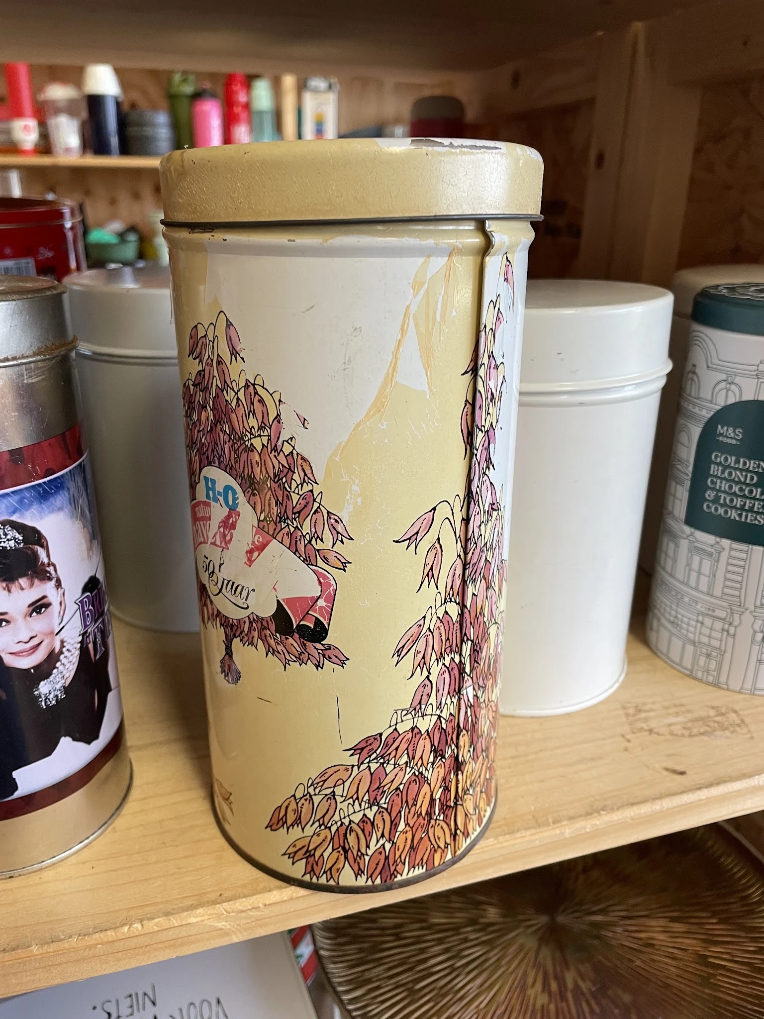 Close-up van een vintage blikken koekjestrommel met illustraties van jonge vrouwen en rozenbotels op een kast met andere huis