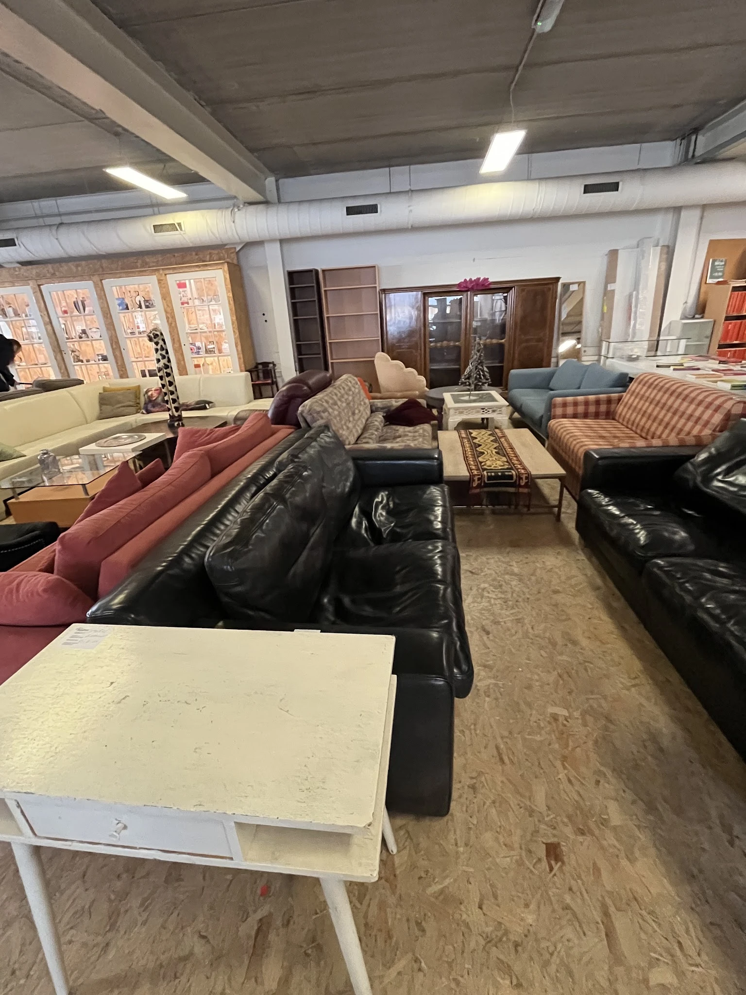 Winkelvloer met diverse zitmeubels: zwarte en gekleurde banken, fauteuils en stoelen uitgestald in de kringloopwinkel