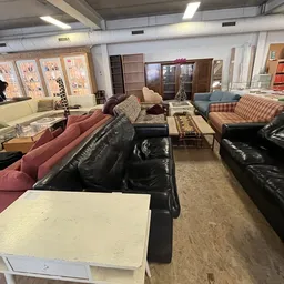 Winkelvloer met diverse zitmeubels: zwarte en gekleurde banken, fauteuils en stoelen uitgestald in de kringloopwinkel
