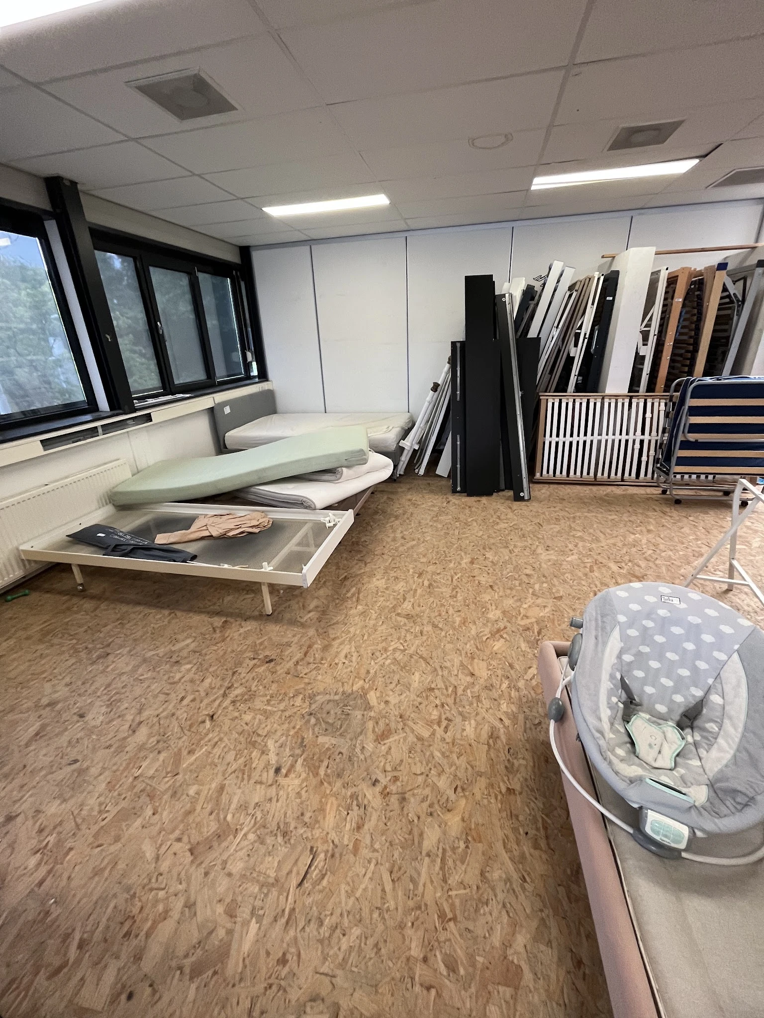 Winkelbinnenruimte met kurkvloer, stellingen met opgeslagen artikelen en een baby-wipstoel op de vloer