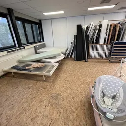 Winkelbinnenruimte met kurkvloer, stellingen met opgeslagen artikelen en een baby-wipstoel op de vloer