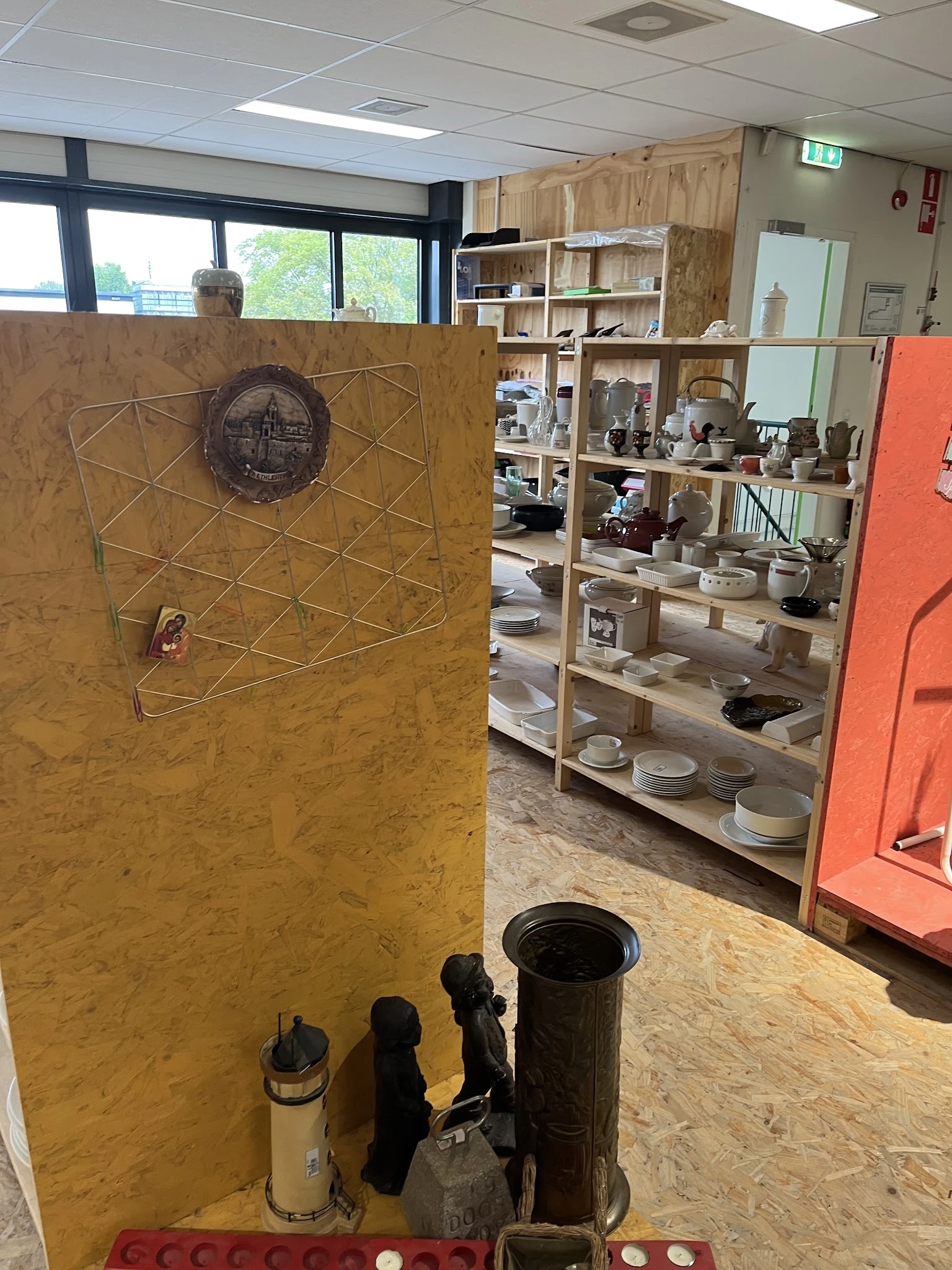 Winkelinterieur met houten stellingen vol serviesgoed en huishoudartikelen, op de voorgrond een geel bord met geometrisch pat