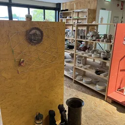 Winkelinterieur met houten stellingen vol serviesgoed en huishoudartikelen, op de voorgrond een geel bord met geometrisch pat