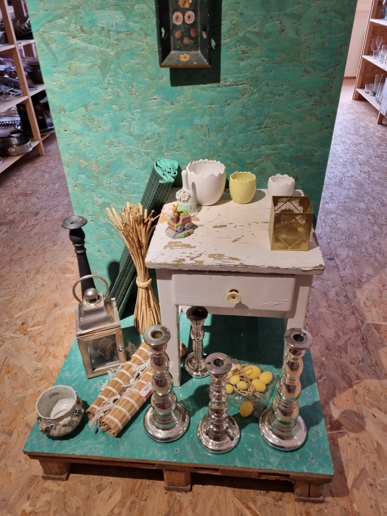 Uitgestalde decoratieve items inclusief kaarsen, vazen, glazen flesjes en gedroogde bloemen op een wit kastje