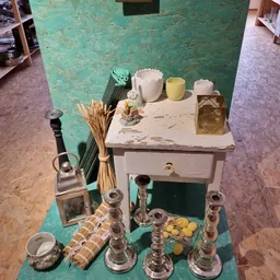 Uitgestalde decoratieve items inclusief kaarsen, vazen, glazen flesjes en gedroogde bloemen op een wit kastje