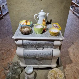 Vintage dressoir met drie laden en decoratieve serviesgoed erop, inclusief theepot en kandelaars