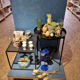 Uitgestalde decoratieve items op zwarte tafeltjes: goudkleurige beeldjes, keramische pot met gele konijnen, groene fles en bl