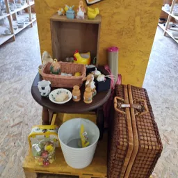 Uitgestalde tweedehands huishoudartikelen op tafel en plank, waaronder manden, servies en decoratieve items.