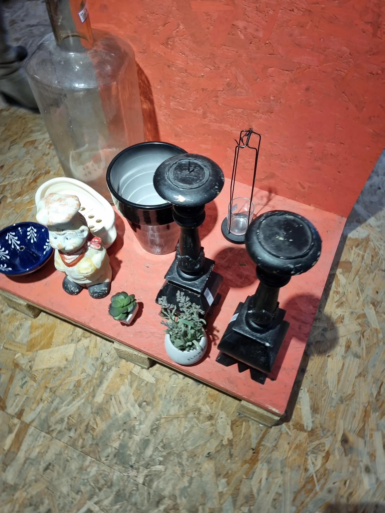 Verzameling tweedehands huishoudartikelen op rode ondergrond: plantenpotten, decoratieve objecten en keukenapparatuur
