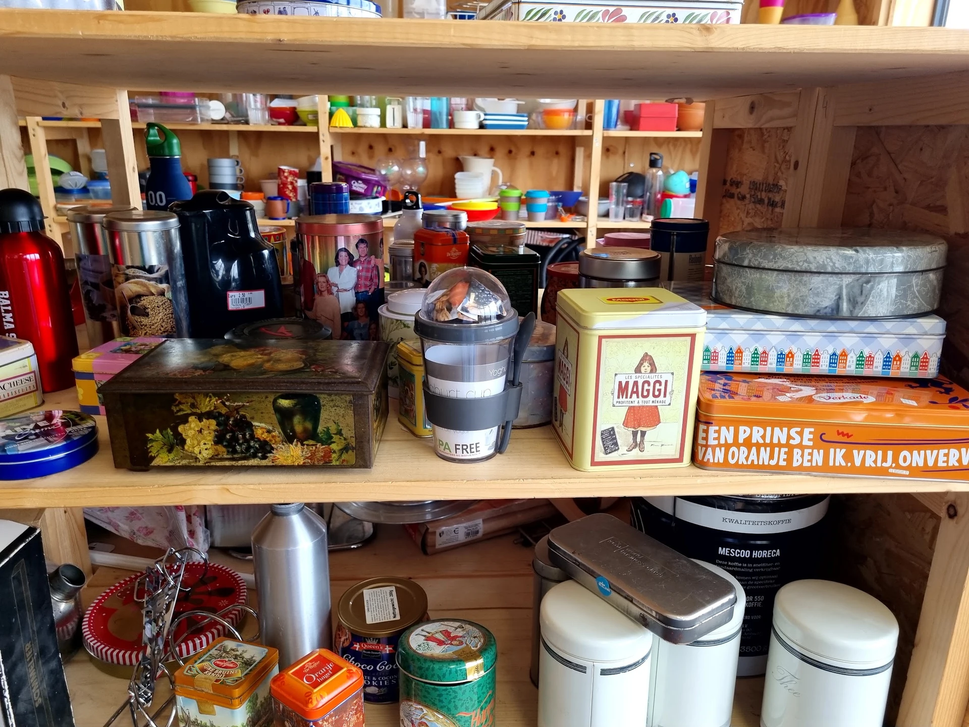 Houten planken vol met tweedehands huishoudartikelen, voedselcontainers, koffiezetapparaten en keukengerei