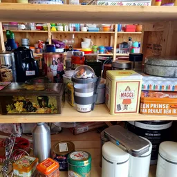 Houten planken vol met tweedehands huishoudartikelen, voedselcontainers, koffiezetapparaten en keukengerei