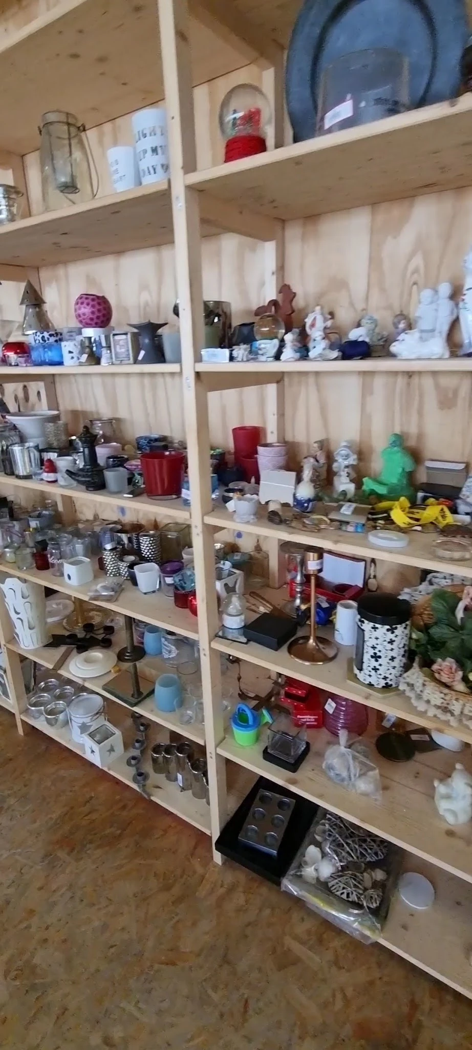 Houten stellingen vol met diverse gebruikte huishoudartikelen, kaarsen, servies en decoraties