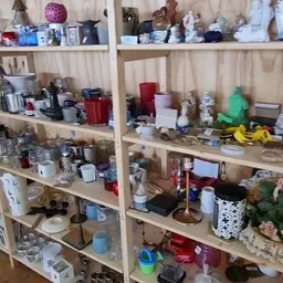 Houten stellingen vol met diverse gebruikte huishoudartikelen, kaarsen, servies en decoraties