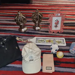 Uitgestalde tweedehandsartikelen op een gestreept tapijt: gouden beeldjes, poloshirt, at&t-pet, portemonnee, boeken en overig