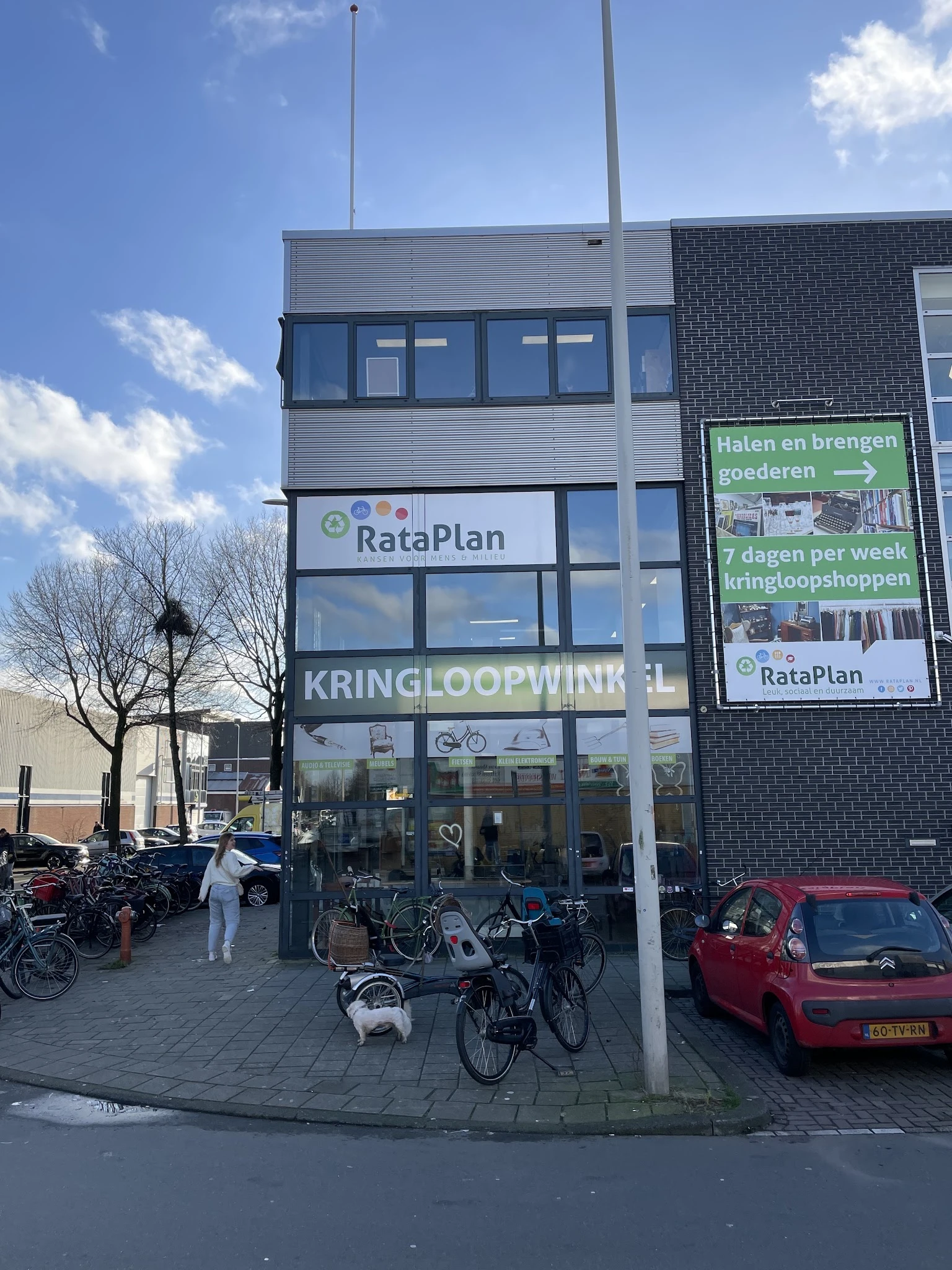 Gevel van kringloopwinkel RataPlan met uithangbord, naam duidelijk zichtbaar, fietsen geparkeerd ervoor