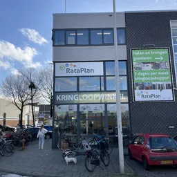 Gevel van kringloopwinkel RataPlan met uithangbord, naam duidelijk zichtbaar, fietsen geparkeerd ervoor