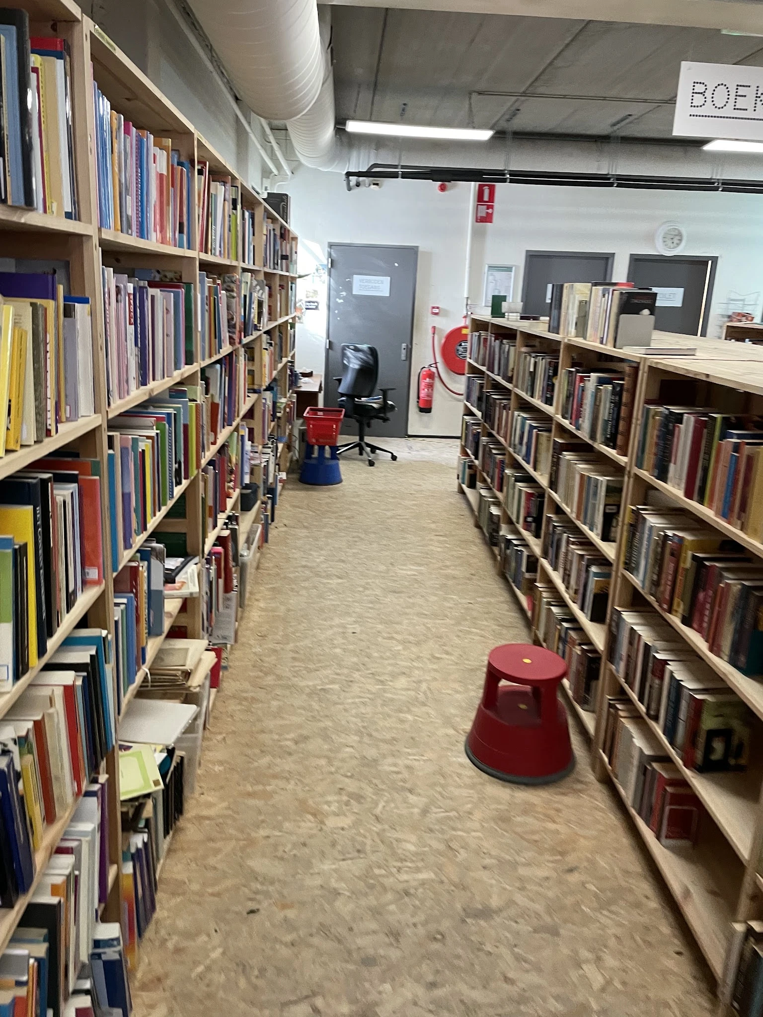 Boekenrekken met dvd's en cd's in een kringloopwinkel, rode krukken op de vloer