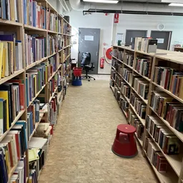 Boekenrekken met dvd's en cd's in een kringloopwinkel, rode krukken op de vloer