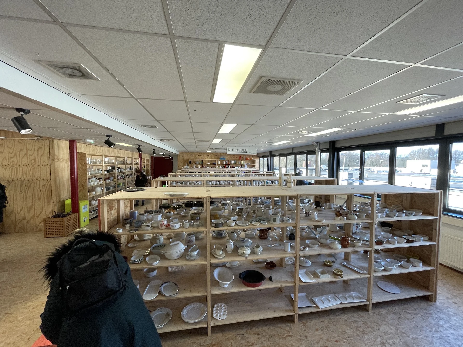 Houten stellingen met aardewerk, servies en huishoudelijke artikelen in de kringloopwinkel