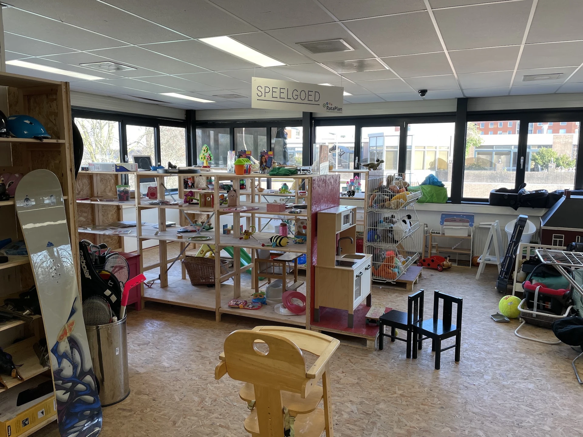 Winkelvloer met stellingen vol speelgoed, boeken en andere artikelen, grote ramen aan de voorkant