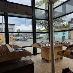 Winkelvloer van kringloopwinkel met houten display-bakken vol boeken, grote ramen en zicht op straat buiten