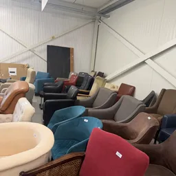 Verzameling tweedehands fauteuils en stoelen in verschillende kleuren en stijlen opgesteld in een magazijn