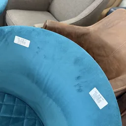 Blauwe ronde poef of zitobject met prijsstickers, naast bruine stoelen