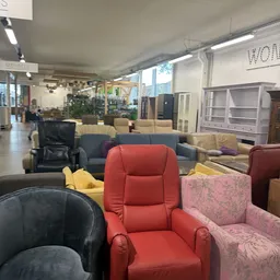 Diverse tweedehands meubels uitgestald in de winkel, waaronder rode fauteuils, blauwe bank en gele kussens
