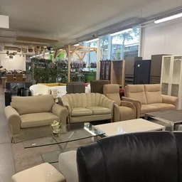 Tweezitsbanken en fauteuils in beige en taupe tonen, uitgestald in de winkelruimte met glazen wand op achtergrond