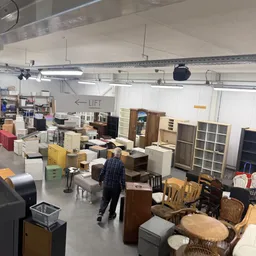 Winkelvloer vol met tweedehands meubilair, kasten, stoelen en huishoudartikelen onder fluorescente verlichting
