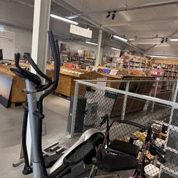Winkelvloer met boekenrekken, een hometrainer op de voorgrond en een afgesloten sectie met kooiwanden in een kringloopwinkel