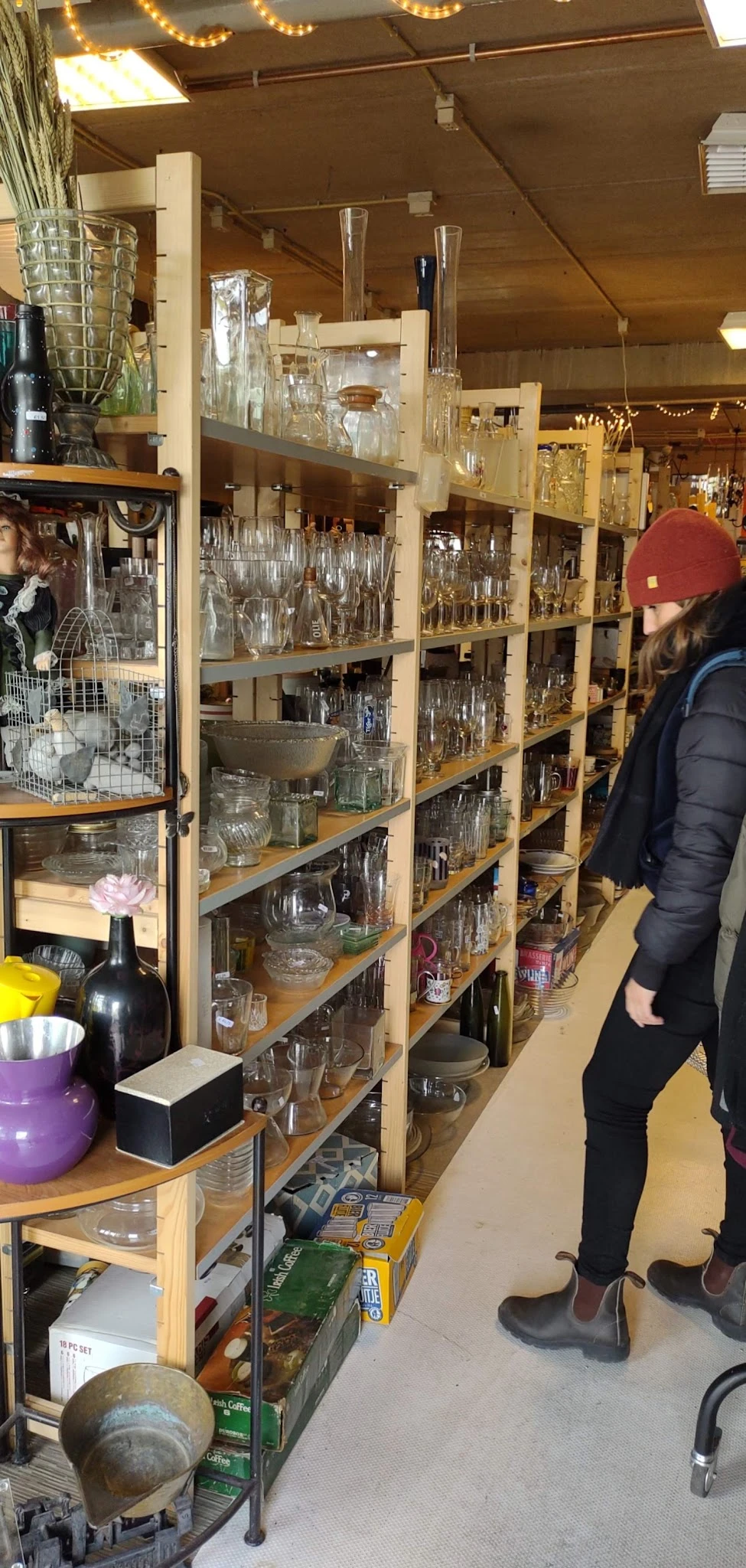 Uitgestalde glazen en drinkglazen in verschillende vormen en maten op houten stellingen in een kringloopwinkel
