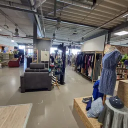 Ruime winkelvloer met kledingrekken, displays en ingerichte zithoeken in een kringloopwinkel