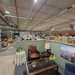 Ingerichte hoek met bruinleren fauteuil, zwarte salontafel, staande lamp en tv in kringloopwinkel