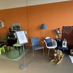Winkelvloer met mogelijk kindermeubilair en speelgoed, oranje wand met verschillende stoelen, lampen en huishoudelijke artike