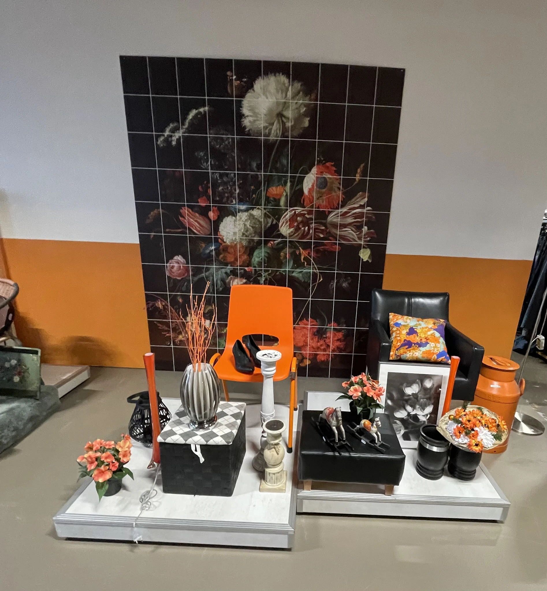 Uitgestalde decoratieartikelen en huisraad: vazen, bloemen, kaarsen, kussens en beeldjes op een tafel met oranje en zwarte ac
