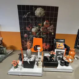 Uitgestalde decoratieartikelen en huisraad: vazen, bloemen, kaarsen, kussens en beeldjes op een tafel met oranje en zwarte ac