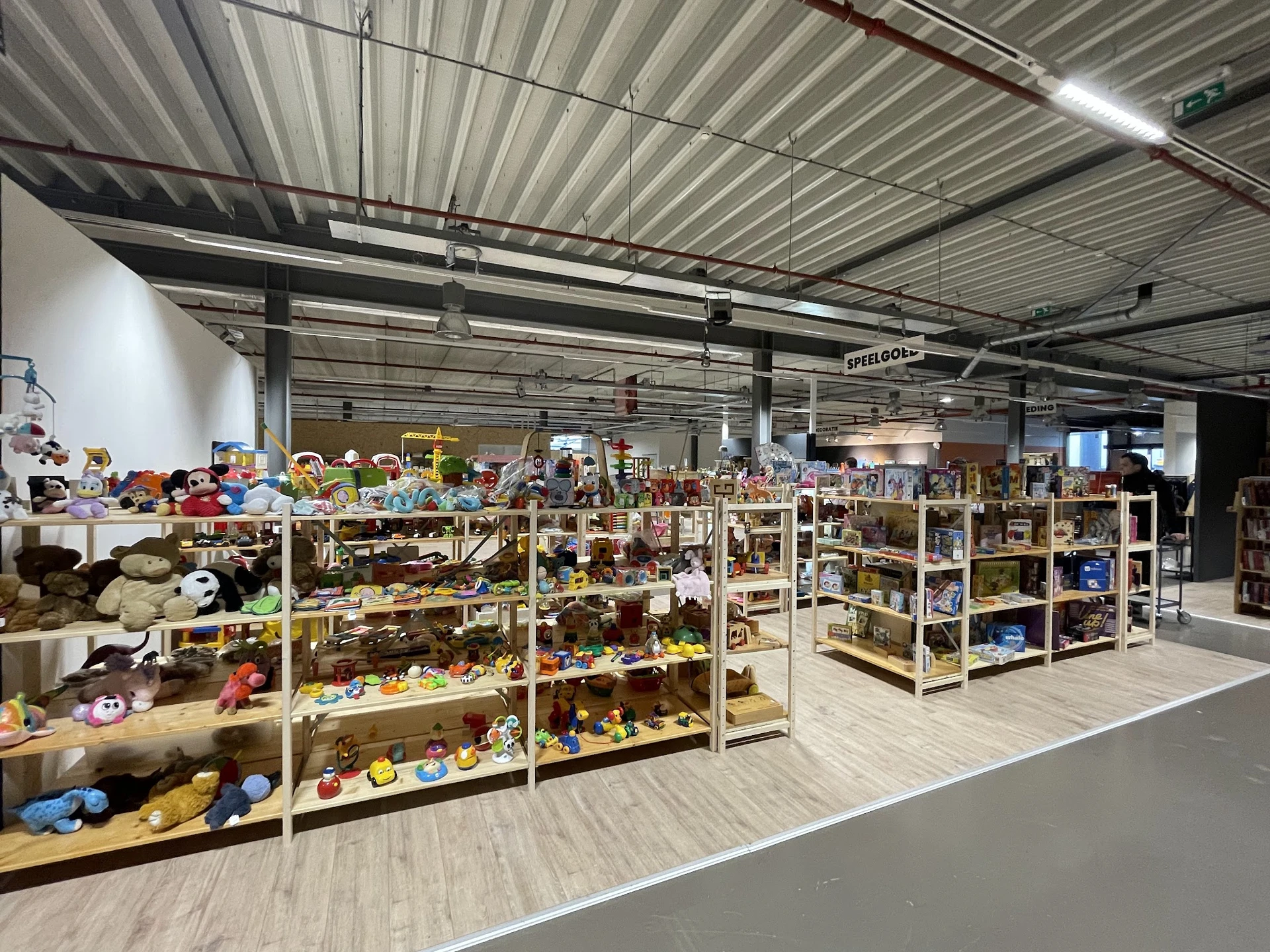 Overzicht van de winkelvloer met houten stellingen vol speelgoed, poppen en diverse tweedehands artikelen
